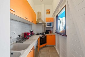 Een compacte keuken met oranje kastjes, een magnetron, een fornuis en een raam met uitzicht op de omgeving.