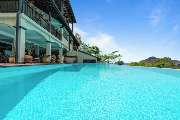 A clear blue pool with a building featuring balconies and potted plants.