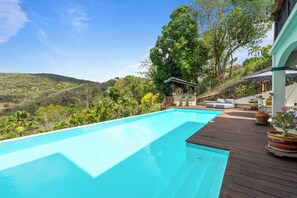 Ein Schwimmbecken mit Holzterrasse, einer kleinen Laube und Blick auf eine hügelige Landschaft.
