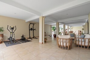 Een ruime binnenruimte met fitnessapparatuur, een zithoek met stoelen en uitzicht op buiten.