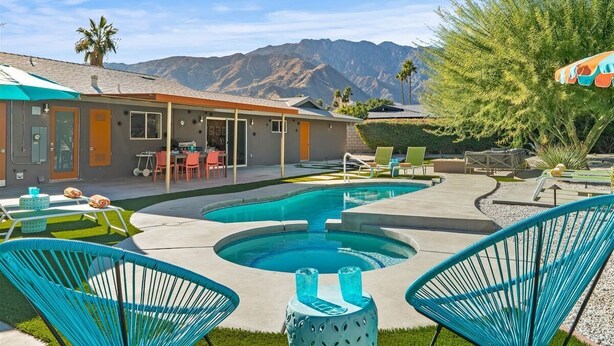 Un espace piscine avec une maison, des sièges d’extérieur et des montagnes en arrière-plan.