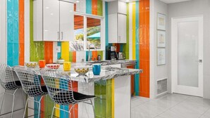 Une cuisine moderne avec des rayures verticales colorées sur les murs, un plan de travail en marbre et des chaises en métal.