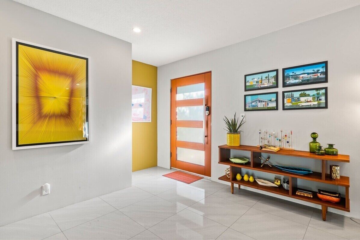 Un couloir moderne agrémenté d’un grand tableau abstrait, d’une console en bois ornée d’objets décoratifs et d’une porte à panneaux de verre.