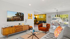 Un salon moderne avec un canapé, un fauteuil et une table basse. Un téléviseur fixé au mur affiche l’image de « PALM SPRINGS ».