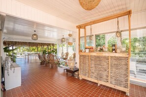 A spacious room with a tiled floor, wicker furniture, and a wooden counter with a view of greenery outside. - Villa Serenity - Four Bedroom Villa, Sleeps 8 (Les Trois-Îlets)