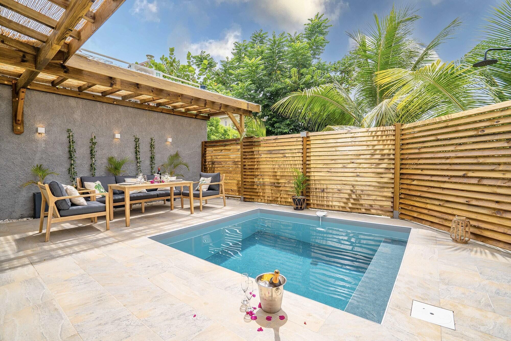 Un área de piscina con una pérgola de madera, asientos y una valla de bambú.