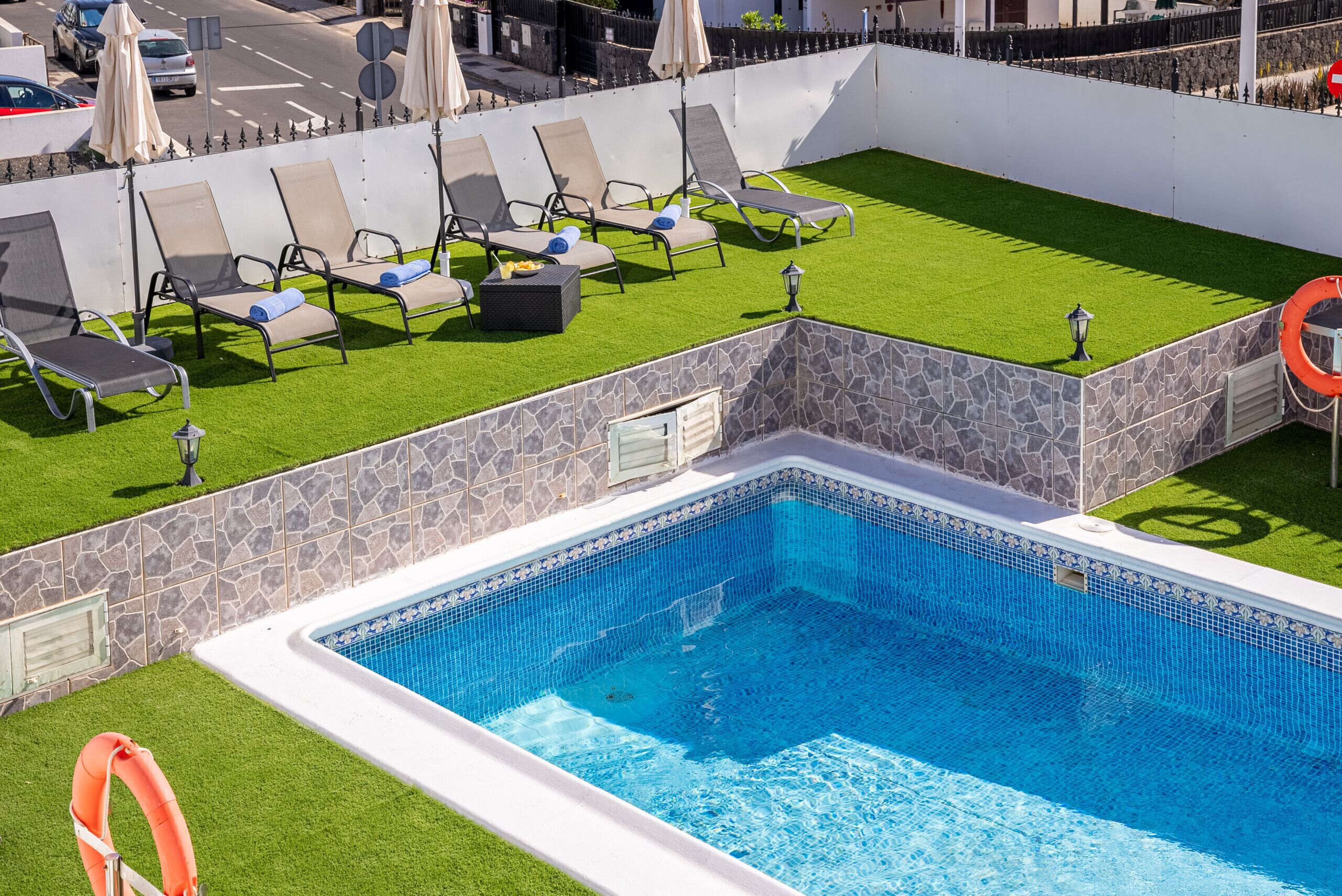A rooftop pool with a clear blue water surface, surrounded by a stone wall and a green artificial lawn.
