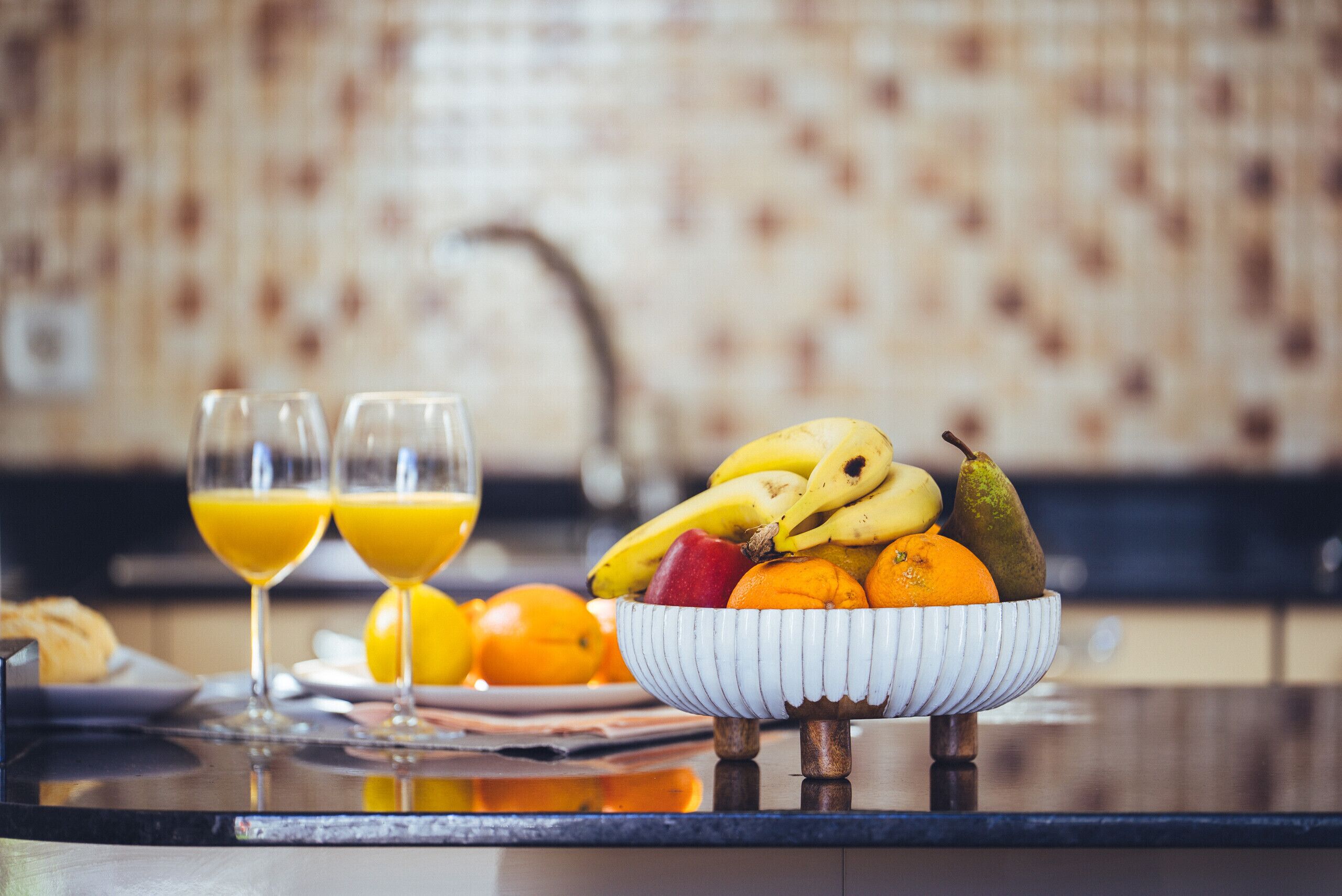 Un desayuno con un bol de fruta, dos vasos de zumo de naranja y un plato de cruasanes.