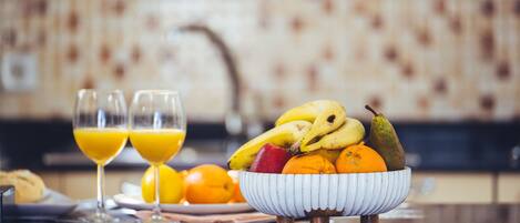 Un desayuno con un bol de fruta, dos vasos de zumo de naranja y un plato de cruasanes.