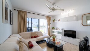 A modern living room with a beige sofa, a glass coffee table, a flat-screen TV, and a ceiling fan. - Casa Monash (Puerto del Carmen)