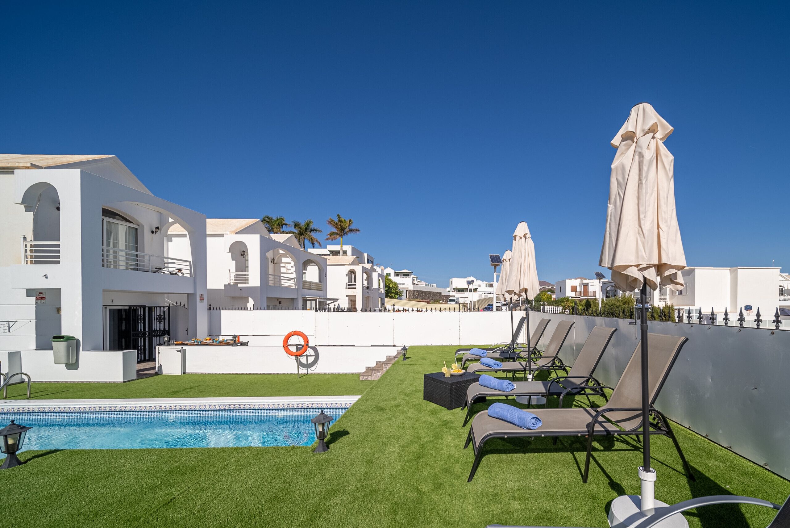 A rooftop pool area with lounge chairs and umbrellas, surrounded by white buildings with arched windows.
