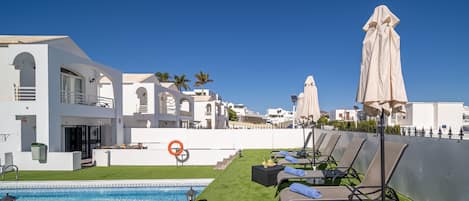 A rooftop pool area with lounge chairs and umbrellas, surrounded by white buildings with arched windows.