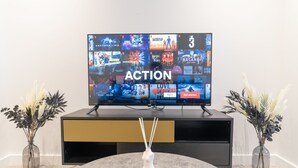 En platt-TV som visar Netflix-gränssnittet med olika serier och filmer, ett träbord med en vit vas och två vaser med torkade växter.