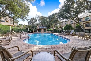 A swimming pool with lounge chairs and a table, surrounded by trees and buildings. - Poolside Oasis: Gated Complex, Near Beach and Pool (Fernandina Beach)
