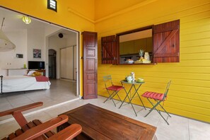 Una habitación con una cama, una mesa de madera y una silla. Hay una puerta que da a otra habitación.