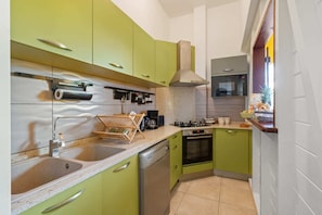Una cocina compacta con gabinetes verdes, un lavamanos de acero inoxidable, un lavavajillas Bosch y una estufa.