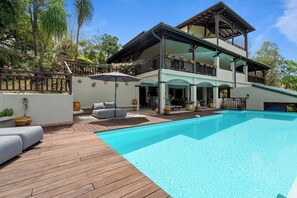 Una casa de dos pisos con piscina, mobiliario exterior y plantas en macetas.