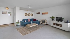 Un salon moderne avec un canapé bleu, une table basse, un téléviseur et un meuble de rangement blanc.