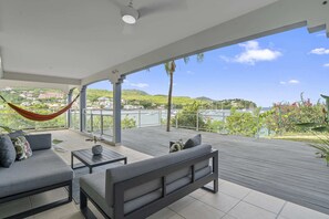 A covered outdoor seating area with a hammock, a sofa, and a table, overlooking a marina and hills. - Appartement Tropical Sunset (Les Trois-Îlets)