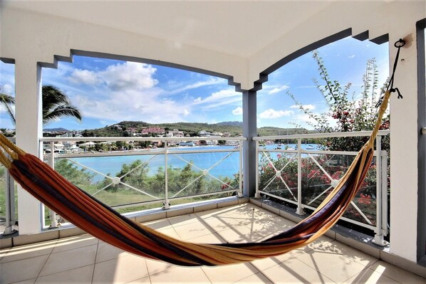 Un balcon avec un hamac, une piscine et une vue sur la ville et les collines.