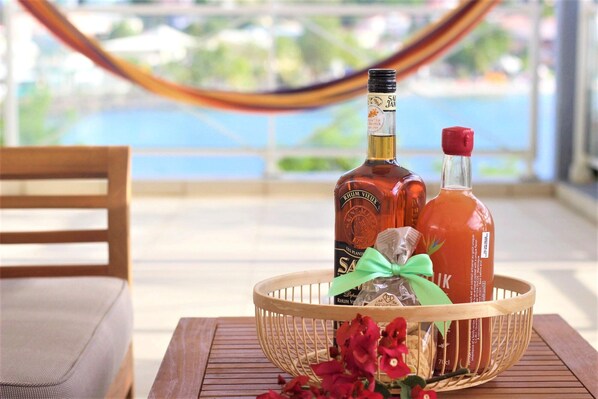 A wooden table with a wicker basket containing two bottles of rum, a wrapped gift, and red flowers.