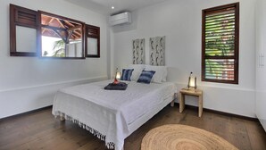 Une chambre à coucher comprenant un lit, une table de chevet, un climatiseur fixé au mur et une fenêtre avec des volets.