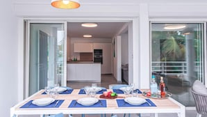 Un comedor con una mesa preparada para cuatro personas, una cocina al fondo y vistas al exterior a través de una puerta de vidrio.