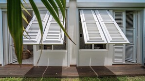 Una casa con contraventanas blancas, una terraza de madera y un pequeño jardín.
