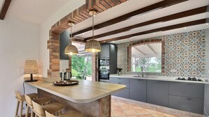 Cocina moderna con una isla central, taburetes de bar, luces colgantes y un salpicadero con diseño.