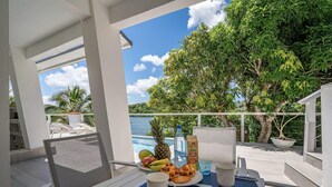 Een balkon met een ontbijttafel, met uitzicht op een zwembad en weelderige begroeiing.
