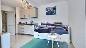 Een knus woongedeelte met een bed, een klein tafeltje met een vaas en een keuken met kastjes en een spoelbak.