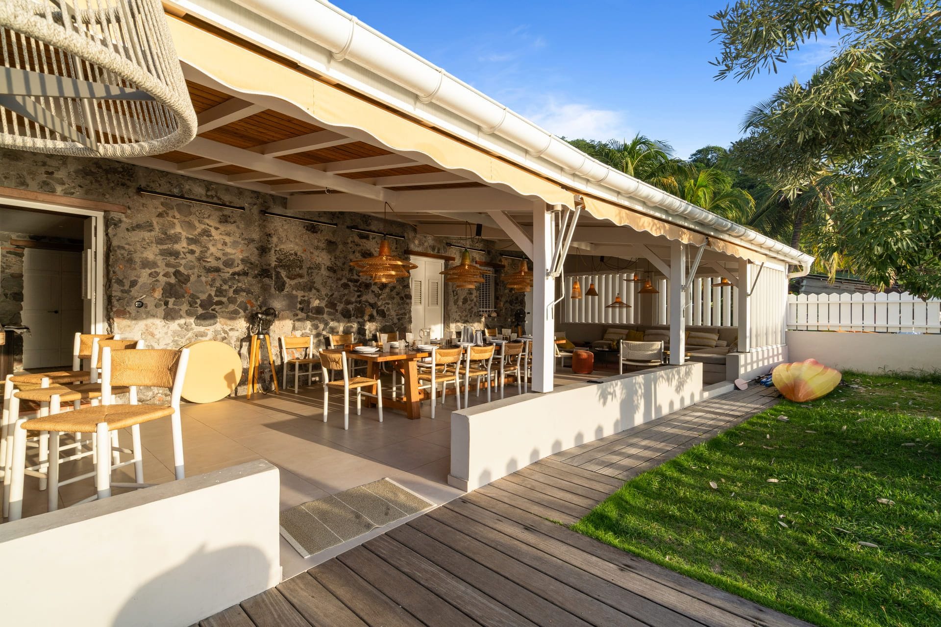 Un espace extérieur aménagé pour les repas, avec des murs en pierre, du mobilier en bois et des luminaires suspendus.