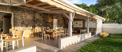 Un espacio para comer al aire libre con paredes de piedra, muebles de madera y luces colgantes.