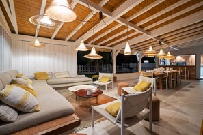 A spacious living area with a high ceiling, wooden beams, and a dining area with a brick wall and modern furniture. - La maison dans la mer (Saint-Pierre)
