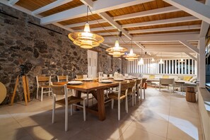 A dining area with a stone wall, wooden ceiling beams, and multiple hanging pendant lights. - La maison dans la mer (Saint-Pierre)