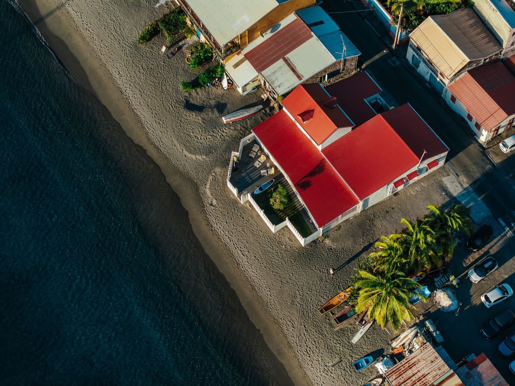 An aerial view of a beachfront property with a red-roofed building, a sandy beach, and a clear view of the ocean.
