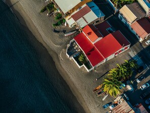 An aerial view of a beachfront property with a red-roofed building, a sandy beach, and a clear view of the ocean. - La maison dans la mer (Saint-Pierre)