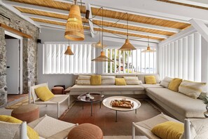 Un salón moderno con pared de piedra, vigas de madera en el techo y ventanas amplias.