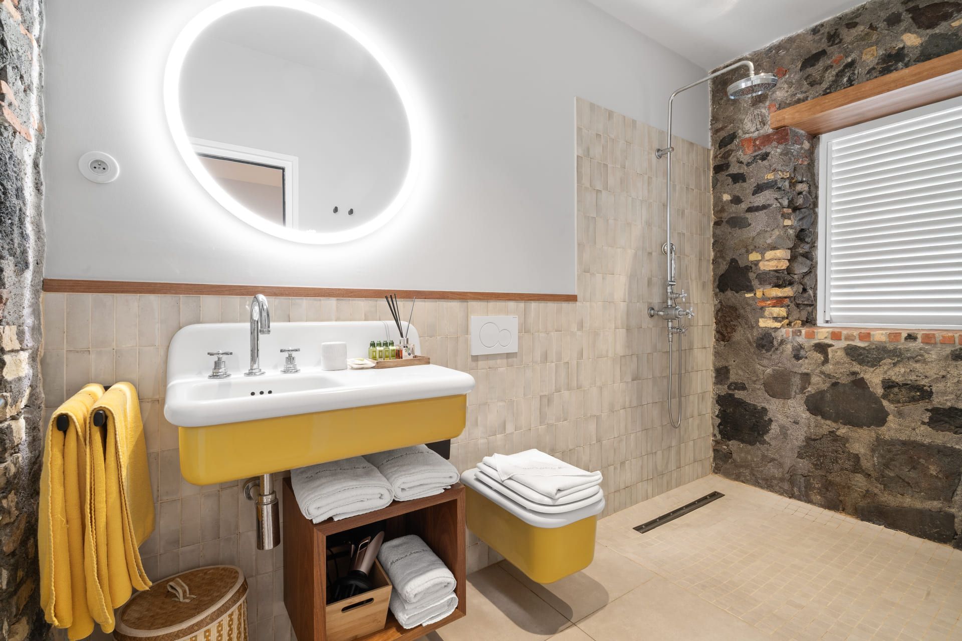 A bathroom with a stone wall, a yellow sink, a mirror, and a shower.