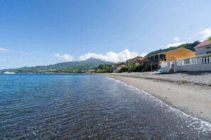 Una spiaggia con acque limpide, una riva sabbiosa e edifici con balconi che si affacciano sul mare.