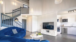 Ein modernes Wohnzimmer mit einem blauen Sofa, einem Flachbildfernseher und einer Küchenzeile mit Mikrowelle und Backofen.