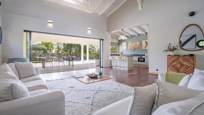 A spacious living area with a large window, a kitchen, and a dining area. - Villa Cactus - Three Bedroom Villa, Sleeps 6 (Le François)