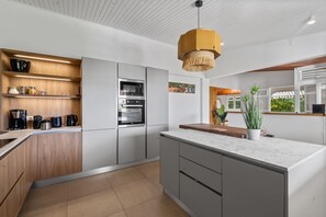 A modern kitchen with a built-in oven, a coffee station, and a large island with a potted plant.