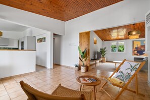 A spacious living area with a wooden ceiling, a dining area with a table and chairs, and a kitchen in the background.