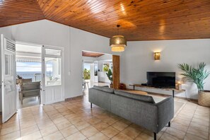 A spacious living area with a grey sofa, a flat-screen TV, and a wooden ceiling.
