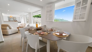 A dining area with a table set for four, white chairs, and a view of greenery outside. - Villa Alexina - Four Bedroom Villa, Sleeps 8 (Le Robert)