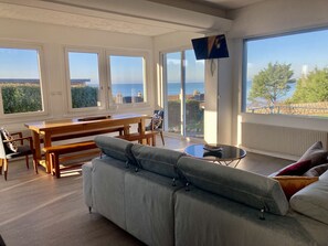 A spacious living room with a large sofa, a wooden dining table, and a TV mounted on the wall. - Les pénates, near beach, picturesque village (Veules-les-Roses)