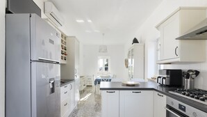 A modern kitchen with white cabinetry, a stainless steel refrigerator, a gas stove, and a dining area with a table and chairs. - Villa Gabriella con Piscina by Wonderful Italy (Ostuni)