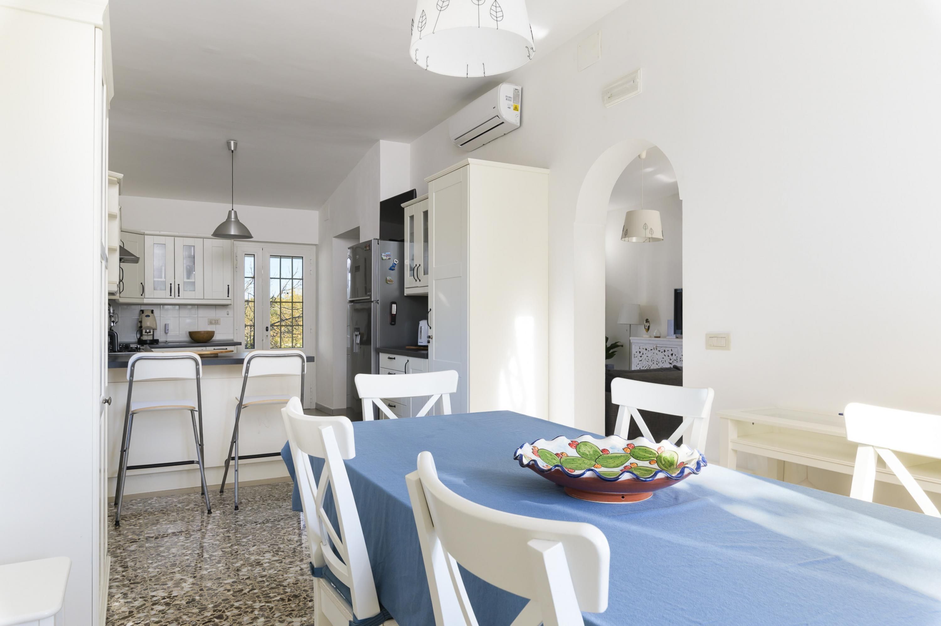 A dining area with a blue tablecloth, white chairs, and a decorative bowl on the table.