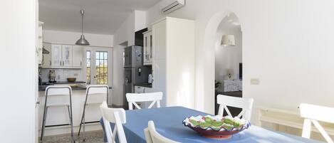 A dining area with a blue tablecloth, white chairs, and a decorative bowl on the table.